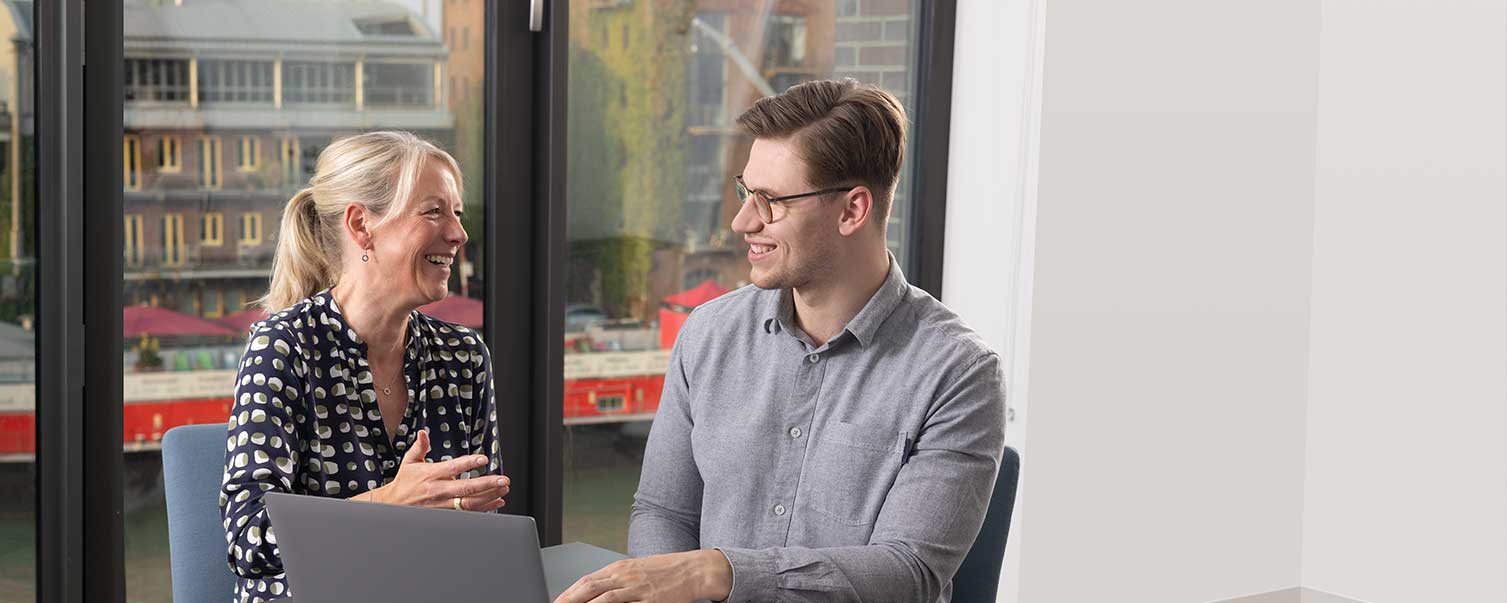 Lachende Frau und Mann sitzen vor einem Laptop im Hintergrund der Stadthafen, Münster